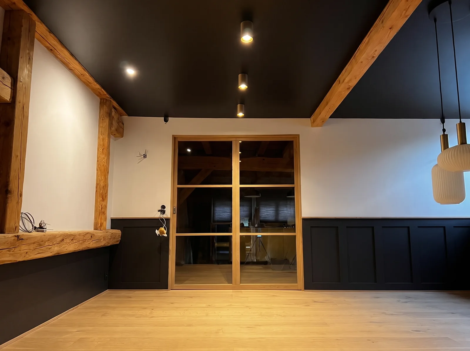 Pièce sous un plafond tendu noir mat entre des poutres en chêne apparentes, spots encastrés